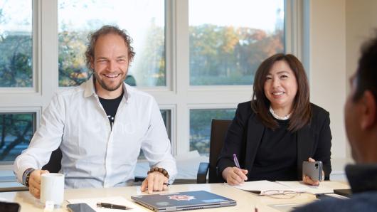 Male and female executive sit engaged at a table listening to their peer speak.