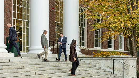 Three male executives and one female executive walk on the steps of Baker Library