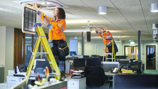 Two workers on ladders changing filters in the ceiling