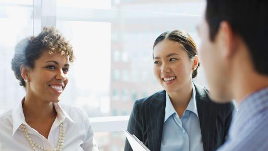 African-American female executive and Asian-American female executive conversing with a male executive