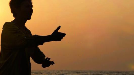 A woman doing tai chi at sunset or sunrise.